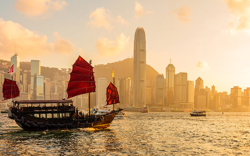 Junk boat sailing past the Hong Kong city skyline at sunset